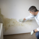 Man with mouth nose mask and blue shirt in front of wall with mold