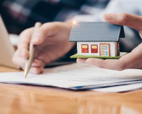 Someone signing a document and holding a house model in their other hand