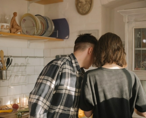 Couple standing in kitchen looking at something in their hand, facing away from camera