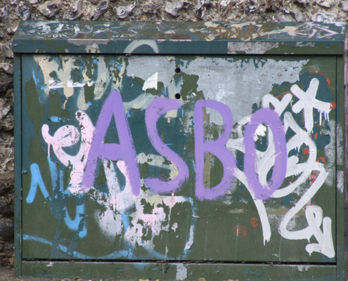 A telephone junction box daubed with graffiti. The box is situated outside the Brighton & Hove School in Hove, Sussex, England. The most prominent tag is "ASBO", short for Anti-Social Behaviour order