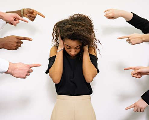 People pointing at a woman with hands over her ears