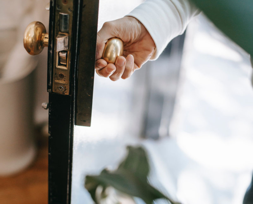 Hand opening a door, with green plants in foreground