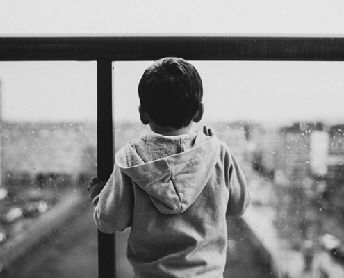 Small boy looking through balcony glass that has rain drops on it