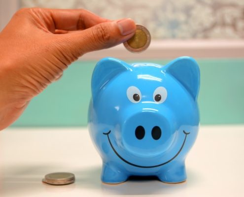 a hand placing a pound coin in a blue porcelain piggy bank