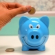 a hand placing a pound coin in a blue porcelain piggy bank