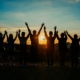 6 people waving their hands up at a sunset
