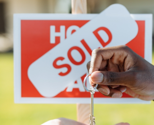 Someone giving a house key to someone behind 'house sold' sign
